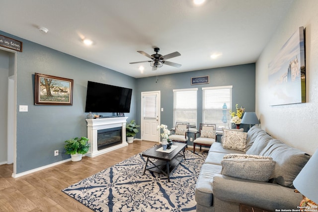 living area featuring ceiling fan, a glass covered fireplace, wood finished floors, and baseboards