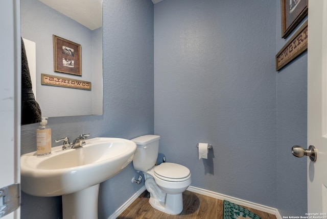 half bath with a textured wall, wood finished floors, toilet, and baseboards