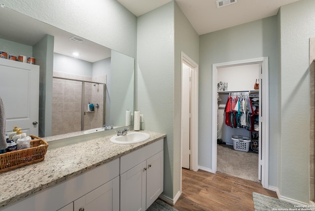 full bath featuring a stall shower, visible vents, wood finished floors, a spacious closet, and vanity