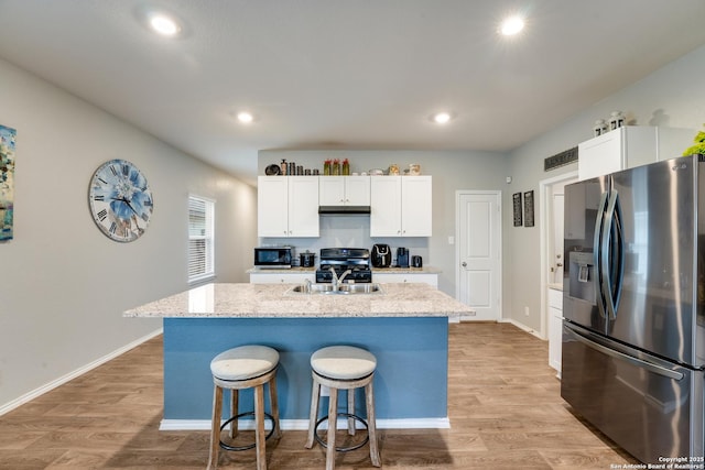 kitchen featuring light wood-style flooring, stainless steel appliances, a sink, white cabinetry, and a kitchen breakfast bar