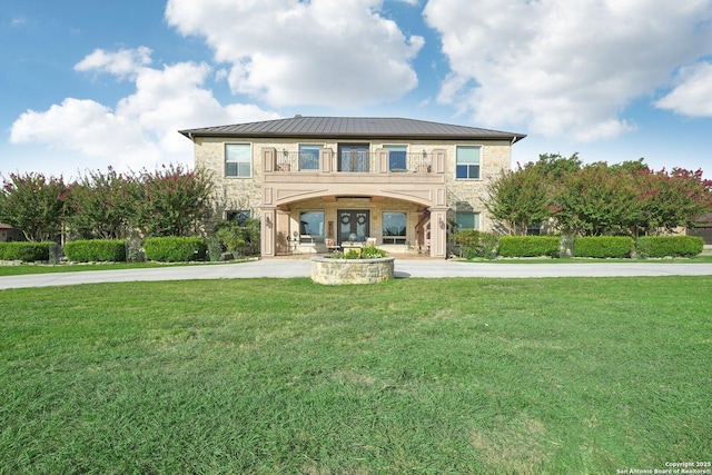 view of front facade with a balcony, a standing seam roof, metal roof, and a front lawn