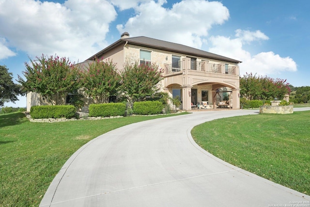 view of front of house with a balcony, concrete driveway, and a front yard