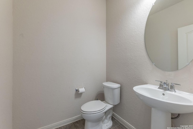 half bathroom with baseboards, a textured wall, toilet, and wood finished floors