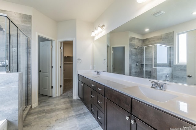 full bath featuring double vanity, a stall shower, a walk in closet, and a sink