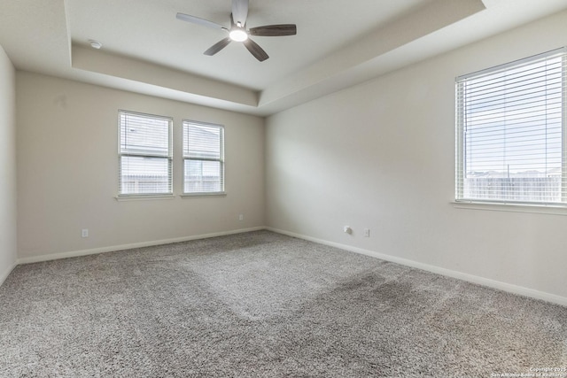 carpeted empty room featuring a raised ceiling, a ceiling fan, and a healthy amount of sunlight