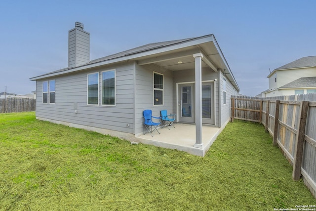 rear view of house featuring a chimney, a lawn, a patio area, and a fenced backyard