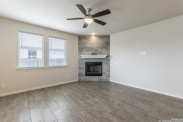 unfurnished living room with a tile fireplace, dark wood-style flooring, ceiling fan, and baseboards