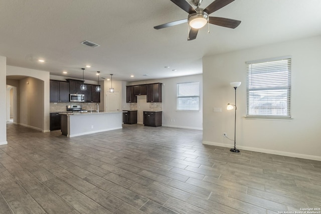 unfurnished living room featuring arched walkways, wood finished floors, visible vents, baseboards, and a ceiling fan