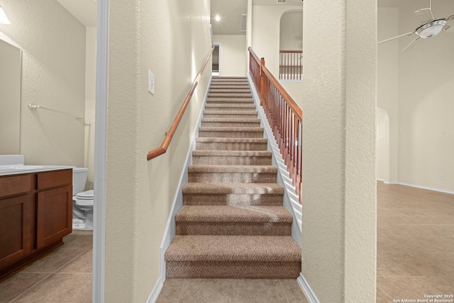 stairs with arched walkways, tile patterned flooring, and baseboards