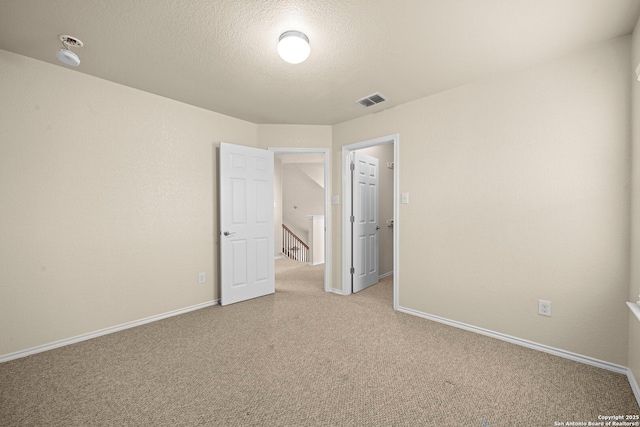 unfurnished bedroom with carpet floors, visible vents, a textured ceiling, and baseboards