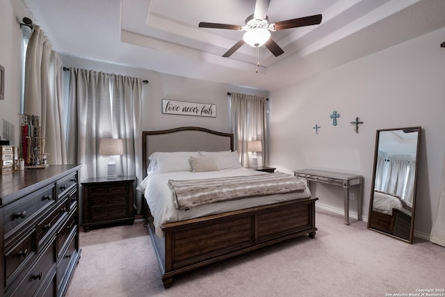 bedroom with light carpet, ceiling fan, a tray ceiling, and baseboards