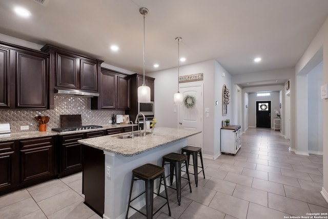 kitchen with tasteful backsplash, a center island with sink, light stone counters, a kitchen bar, and a sink