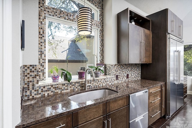 kitchen featuring tasteful backsplash, stainless steel appliances, a sink, dark brown cabinetry, and dark stone counters