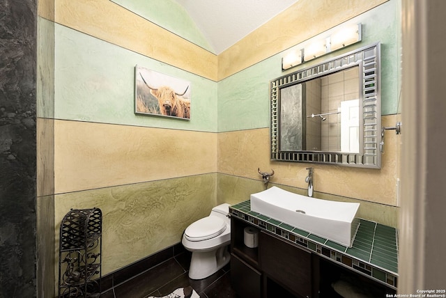 full bathroom featuring tile walls, lofted ceiling, toilet, vanity, and tile patterned flooring