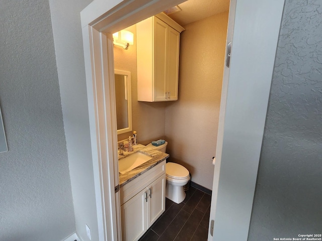 half bath with a textured wall, toilet, wood finished floors, vanity, and baseboards