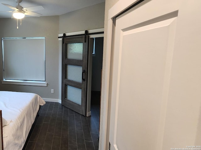 unfurnished bedroom with ceiling fan, a barn door, and dark wood finished floors