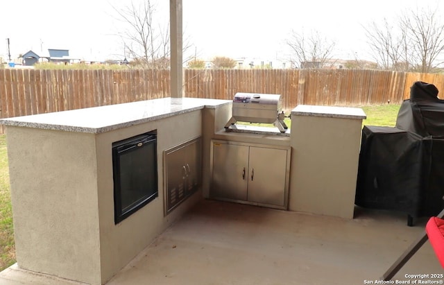 view of patio with a grill, fence, and an outdoor kitchen