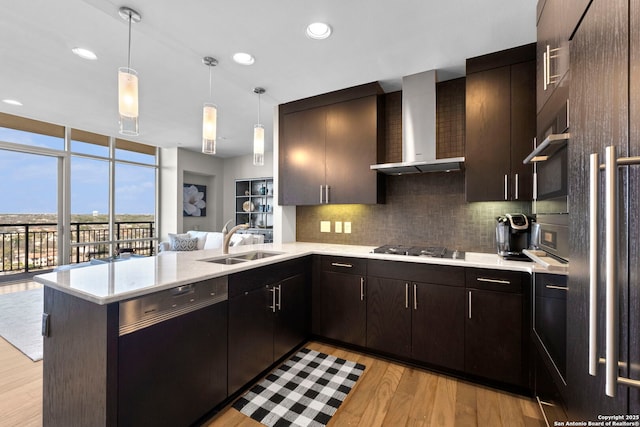 kitchen with floor to ceiling windows, stainless steel appliances, tasteful backsplash, a sink, and wall chimney range hood