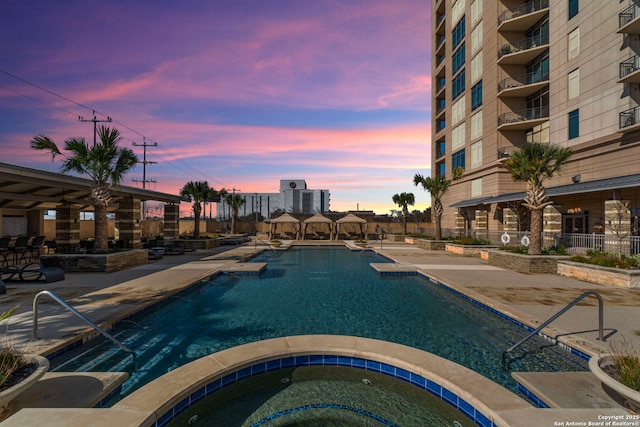 community pool with a patio area, fence, and a hot tub