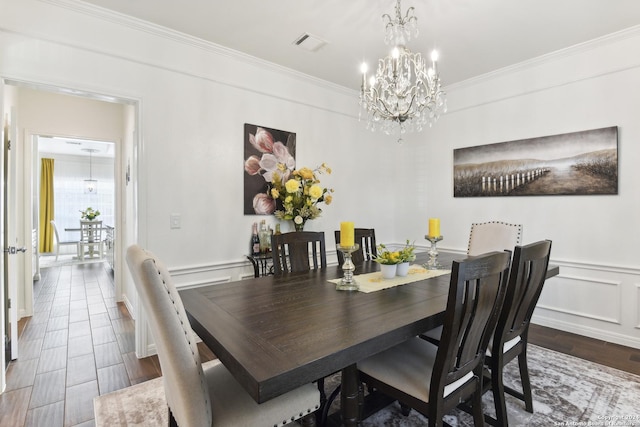 dining area featuring a chandelier, a decorative wall, visible vents, and crown molding