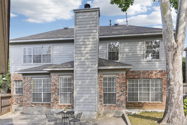 back of property with brick siding, a patio, a chimney, a shingled roof, and fence