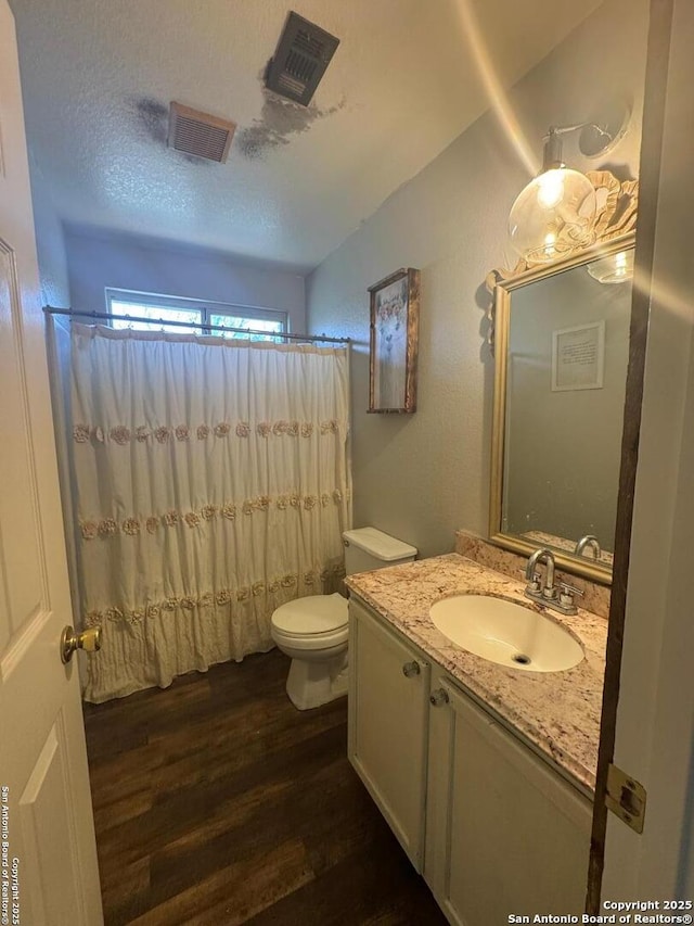 full bathroom featuring a textured ceiling, toilet, wood finished floors, vanity, and visible vents