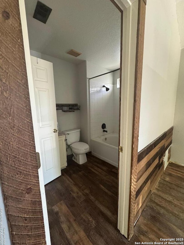 bathroom featuring visible vents, toilet, shower / tub combination, wood finished floors, and a textured ceiling