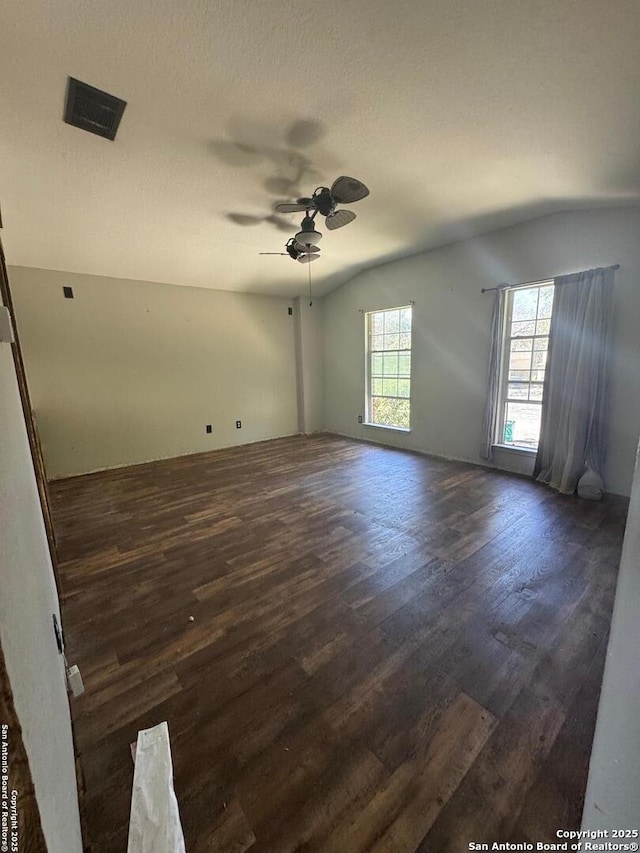 empty room featuring a textured ceiling, lofted ceiling, visible vents, a ceiling fan, and dark wood-style floors