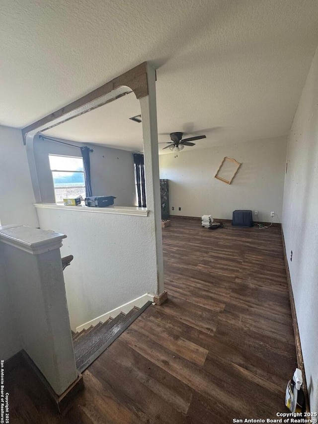 hallway with a textured ceiling, baseboards, wood finished floors, and an upstairs landing