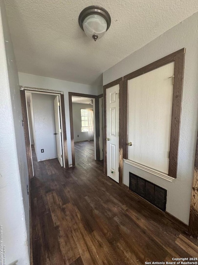 corridor featuring dark wood-type flooring, visible vents, and a textured ceiling