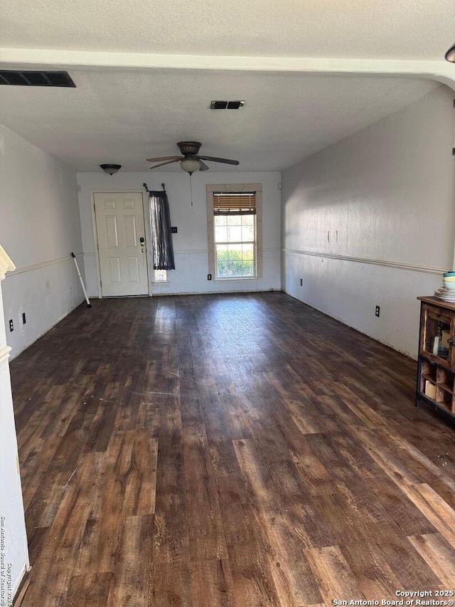 unfurnished living room featuring a ceiling fan, visible vents, dark wood finished floors, and a textured ceiling