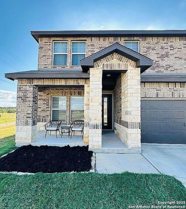 entrance to property featuring a porch, a garage, brick siding, stone siding, and concrete driveway