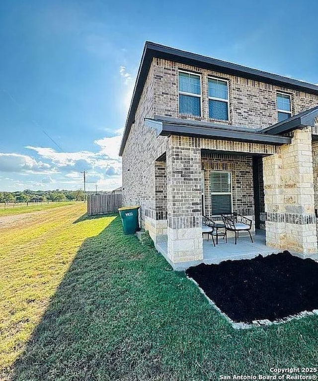 view of home's exterior featuring brick siding, stone siding, a lawn, and a patio