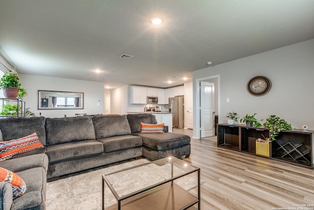 living area with a textured ceiling, light wood finished floors, visible vents, and recessed lighting