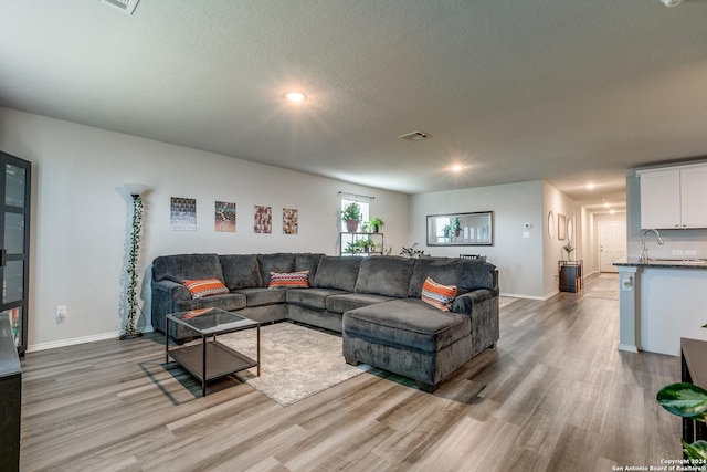 living room with visible vents, a textured ceiling, light wood-style flooring, and baseboards