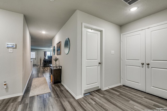 hallway with visible vents, a textured ceiling, baseboards, and wood finished floors