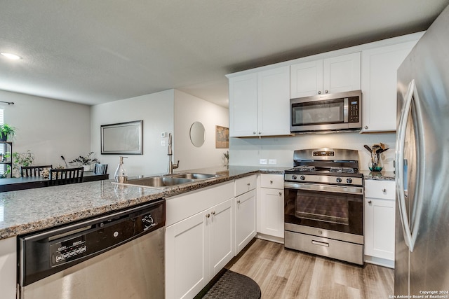 kitchen with light wood finished floors, white cabinets, light stone countertops, stainless steel appliances, and a sink
