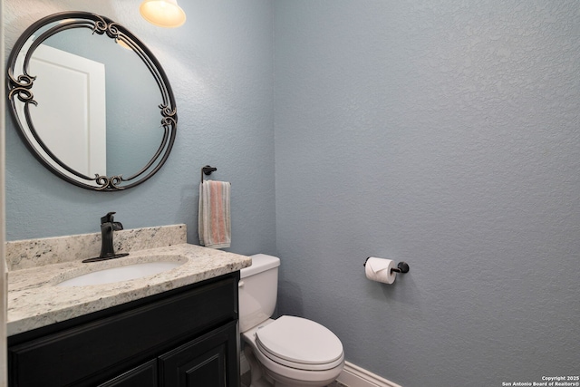 bathroom featuring toilet, a textured wall, and vanity