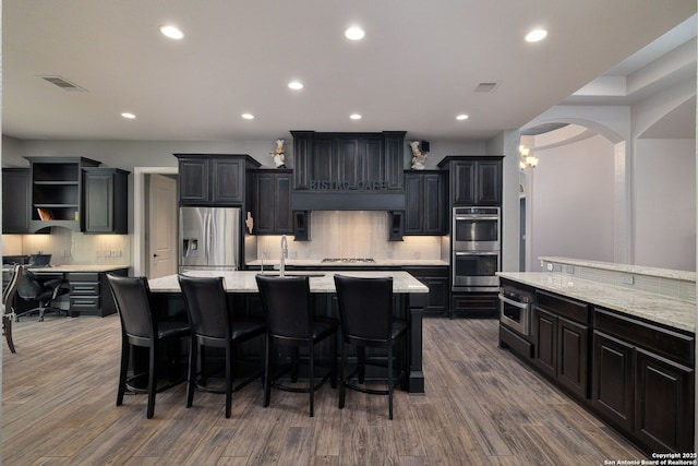 kitchen featuring a center island with sink, stainless steel appliances, visible vents, a sink, and dark cabinets