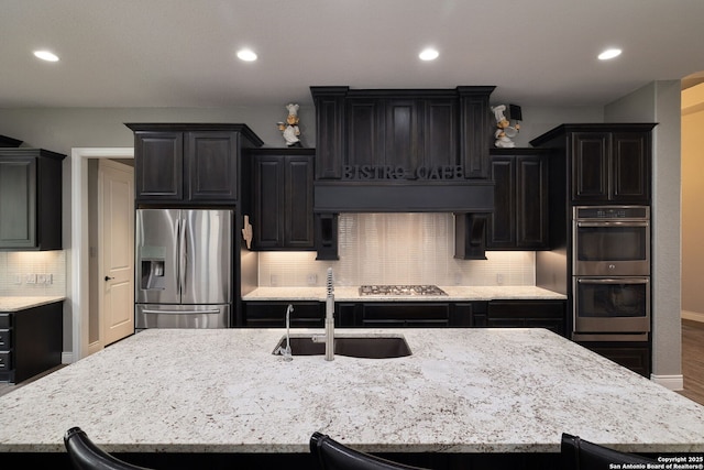 kitchen featuring dark cabinets, a sink, appliances with stainless steel finishes, tasteful backsplash, and an island with sink