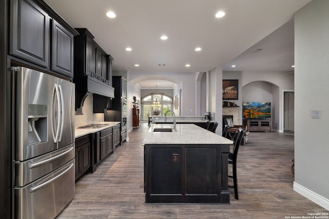 kitchen with arched walkways, a breakfast bar area, stainless steel appliances, a sink, and light stone countertops