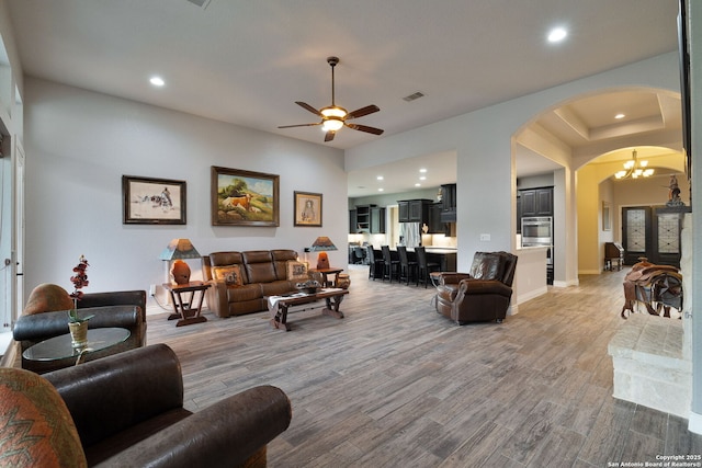 living area featuring arched walkways, light wood finished floors, visible vents, and recessed lighting