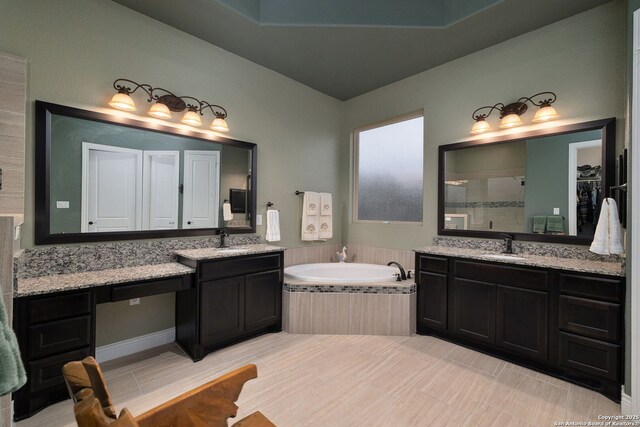 bathroom featuring a garden tub, a shower stall, two vanities, and a sink