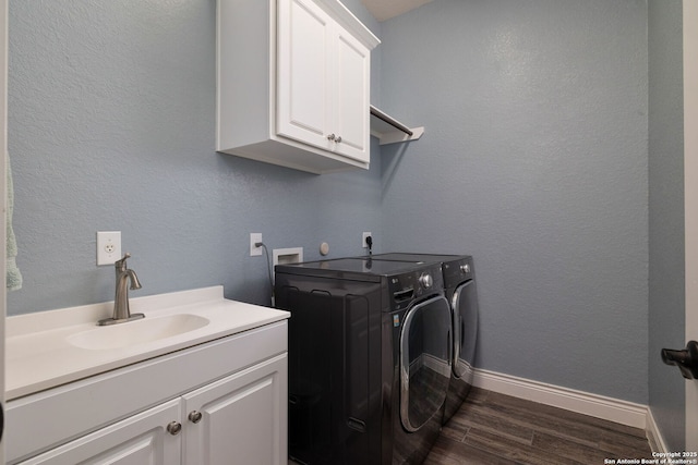 washroom with cabinet space, baseboards, dark wood-style flooring, washer and dryer, and a sink