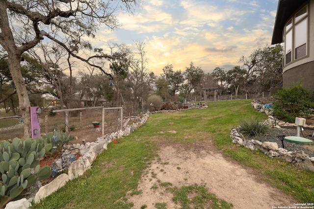 yard at dusk with a vegetable garden and fence