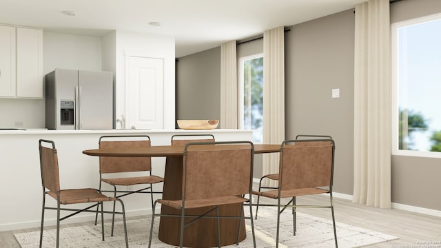 kitchen featuring light countertops, light wood-style flooring, white cabinetry, refrigerator with ice dispenser, and a kitchen breakfast bar