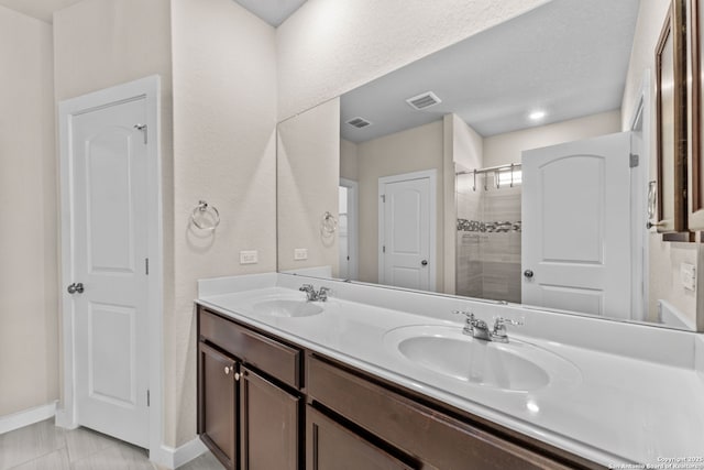 bathroom featuring a tile shower, double vanity, a sink, and visible vents