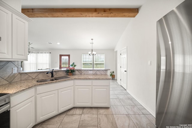 kitchen with a peninsula, a sink, white cabinetry, freestanding refrigerator, and decorative backsplash