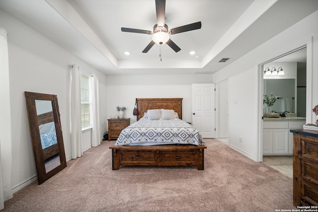 bedroom featuring ensuite bathroom, light carpet, visible vents, baseboards, and a tray ceiling