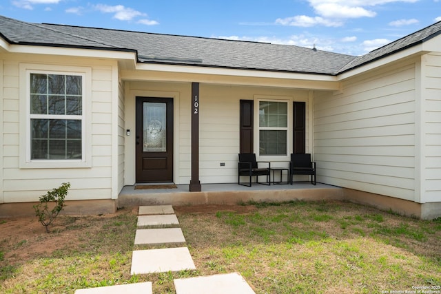 doorway to property with covered porch, a shingled roof, and a yard